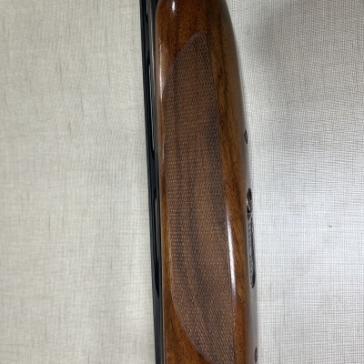 Parte de madeira polida e entalhada de uma arma com detalhes em metal escuro