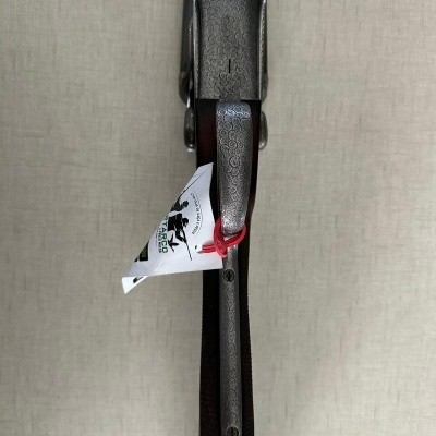 Espingarda com coronha de madeira e partes metálicas gravadas, vista de cima, com etiqueta branca presa