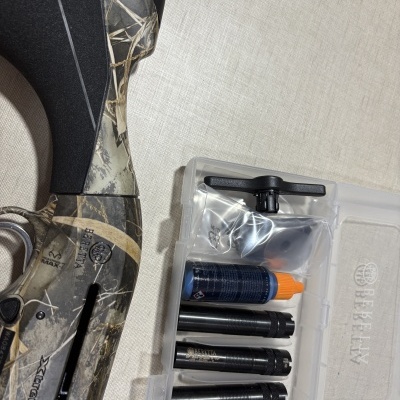 Espingarda Beretta camuflada e estojo transparente com acessórios e frasco azul