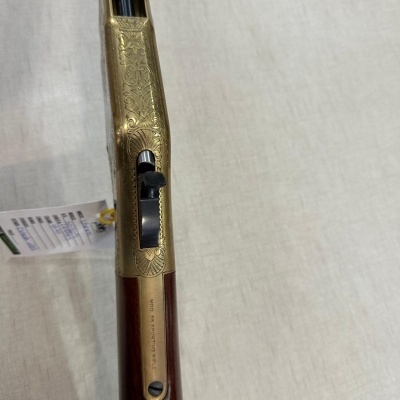 Espingarda dourada gravada com cabo de madeira castanha sobre superfície clara