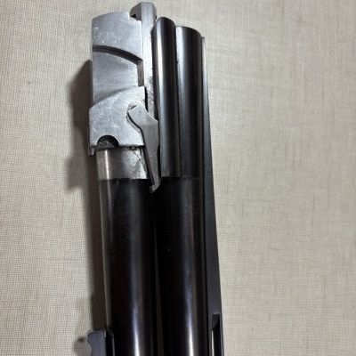 Parte superior de cano duplo metálico preto e prateado em fundo bege.
