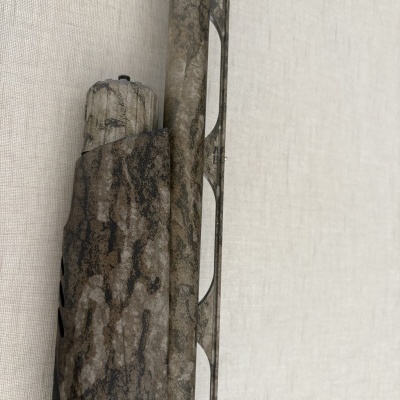 Arma de caça camuflada numa parede branca texturizada