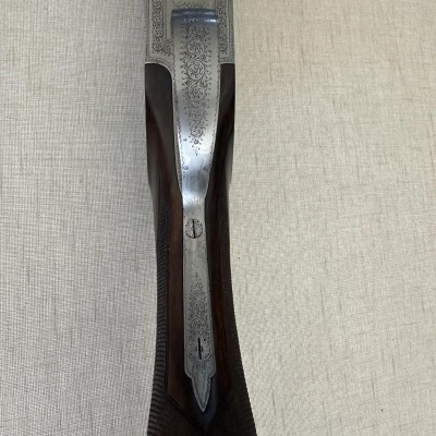 Detalhe de espingarda com madeira escura e metal gravado