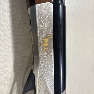 Espingarda com cabo de madeira castanha, metal prateado gravado e detalhes dourados, cano preto.