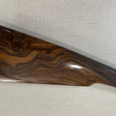 Parte traseira de uma arma de fogo em madeira com veios naturais