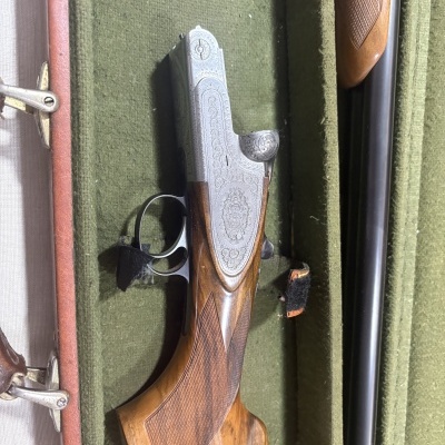 Espingarda de canos paralelos com madeira trabalhada e metal gravado numa caixa verde