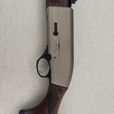 Corpo e coronha de espingarda com madeira e metal cinza claro com gravação em fundo cinza.