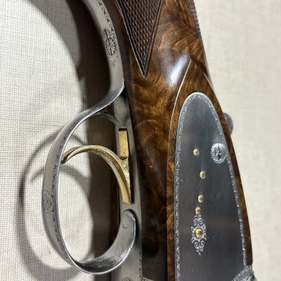 Detalhe de caça ou espingarda com metal gravado e empunhadura em madeira.