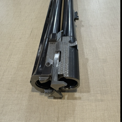 Cano duplo metálico de espingarda sobre superfície bege texturizada