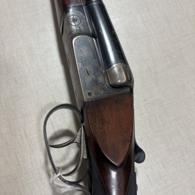 Espingarda dupla com detalhes em madeira e metal sobre superfície bege