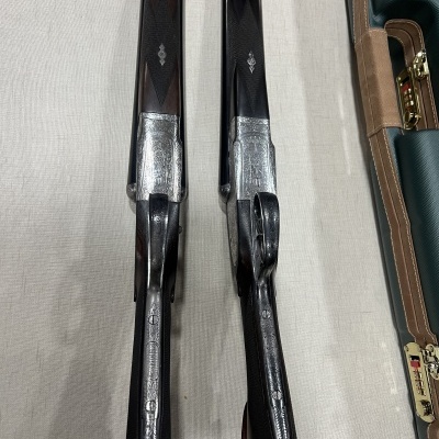 Dois rifles com detalhes em madeira e metal, ao lado de uma mala de transporte