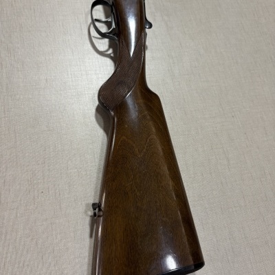 Parte traseira de espingarda de caça em madeira polida e metal prateado com gravação.