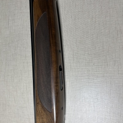 Arma de fogo com empunhadura em madeira e parte metálica preta sobre tecido cinza