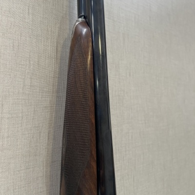 Espingarda de cano duplo com coronha em madeira e canos pretos contra parede bege.