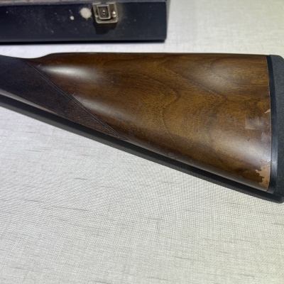 Coronha de espingarda em madeira castanha com almofada preta sobre superfície clara