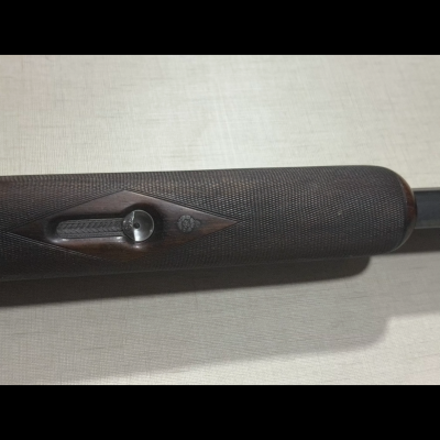 Punho de espingarda em madeira escura com botão metálico e detalhe em relevo