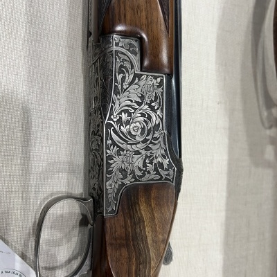 Espingarda de madeira e metal com gravações florais em fundo branco texturizado