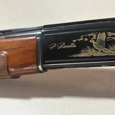 Arma de caça com empunhadura em madeira e caixa preta com gravação dourada de um faisão e texto P. Beretta