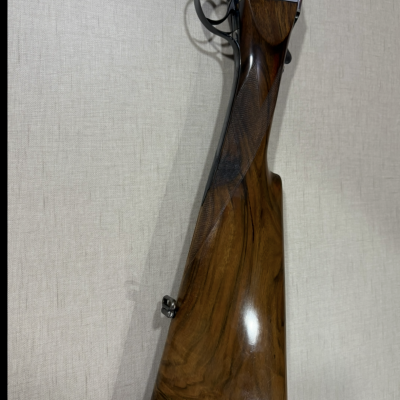 Espingarda com coronha de madeira e parte metálica apoiada numa superfície de tecido beige.