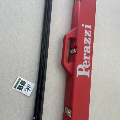 Mala vermelha Perazzi com alça e peça preta longa ao lado sobre superfície clara