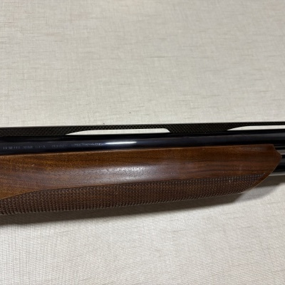 Parte de espingarda com madeira castanha e metal preto com gravação Benelli