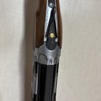 Parte superior de espingarda com decoração engravada e coronha de madeira castanha.