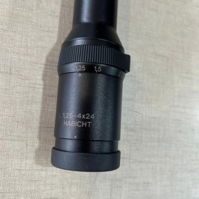 Luneta preta metálica com inscrições e anel de ajuste sobre superfície clara