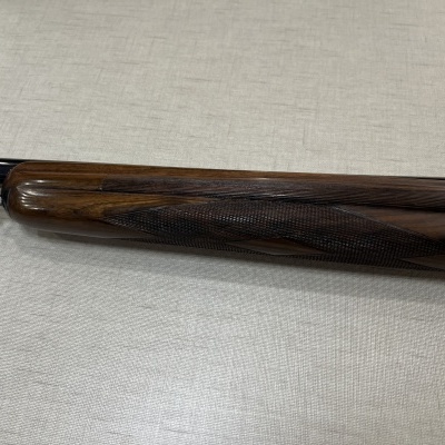 Parte da coronha de madeira e parte metálica de uma arma de fogo sobre uma superfície clara