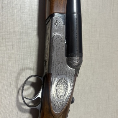 Espingarda de caça com acabamento em madeira e metal gravado sobre fundo bege