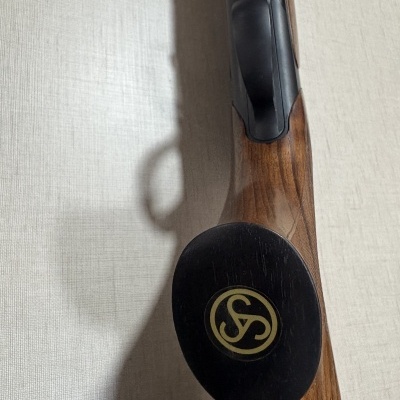 Detalhe de arma de fogo com coronha de madeira castanha e botão decorado.