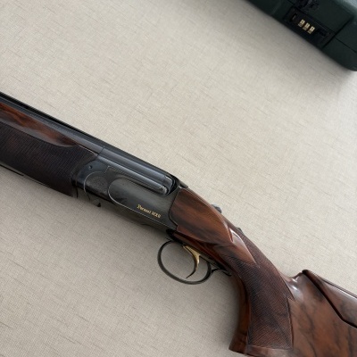 Espingarda Perazzi MX8 em madeira e metal sobre superfície clara com caixa verde ao lado