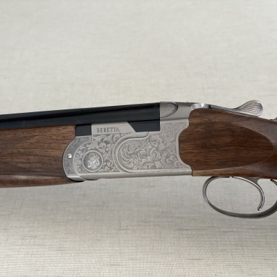 Espingarda Beretta com coronha de madeira escura e corpo metálico prateado com gravura floral.