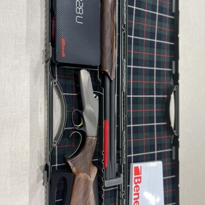 Espingarda desmontada em estojo com padrão xadrez e caixa preta com texto Benelli