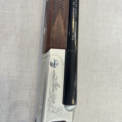 Espingarda com empunhadura em madeira, cano preto e corpo metálico gravado.