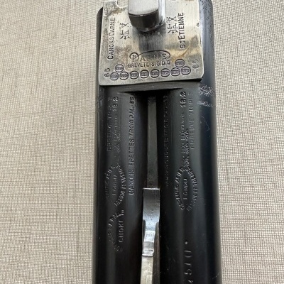 Espingarda de canos sobrepostos em metal preto com apoio metálico e inscrições visíveis