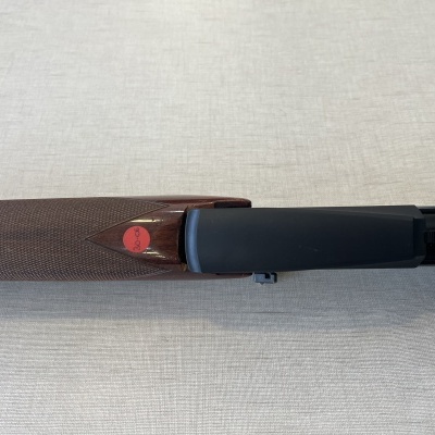 Espingarda com coronha de madeira castanha e detalhes pretos sobre tecido bege claro