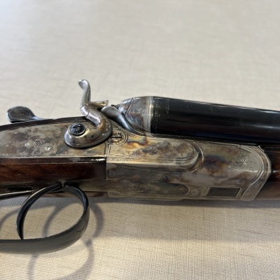 Espingarda dupla com coronha em madeira e acabamento metálico sobre superfície clara