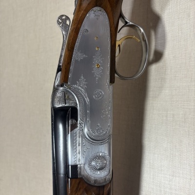 Parte lateral de uma espingarda caça com cabo de madeira e corpo metálico com gravações e texto P. Beretta