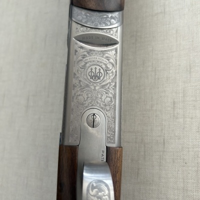 Arma de caça com punho em madeira escura e metal gravado, texto MADE IN ITALY e 686 SILVER PIGEON