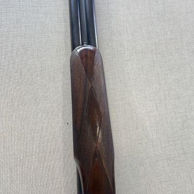 Arma de fogo com canos pretos e empunhadura de madeira escura em tecido cinzento