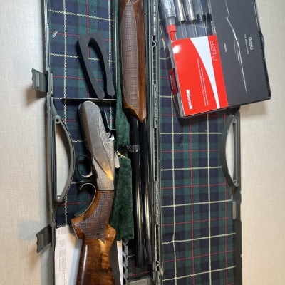 Espingarda desmontada com acessórios numa mala cinzenta forrada a padrão tartan