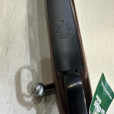 Espingarda em madeira castanha e metal preto com logotipo Lawser sobre tecido bege