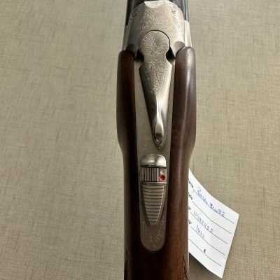 Espingarda clássica com madeira e metal gravado em fundo bege.