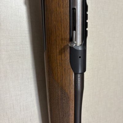 Parcial de rifle com coronha em madeira castanha e parte do cano metálico prateado e preto