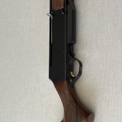 Arma de fogo com cabo em madeira castanha e corpo metálico preto num fundo bege.