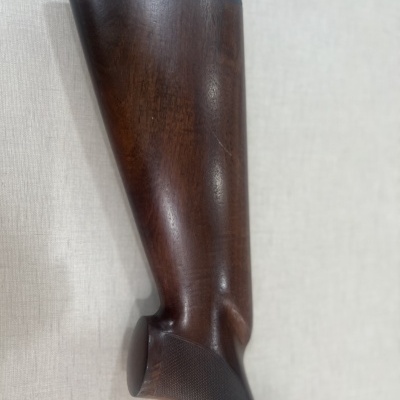 Coronha de arma de fogo em madeira escura com textura fina na pega e acabamento polido.