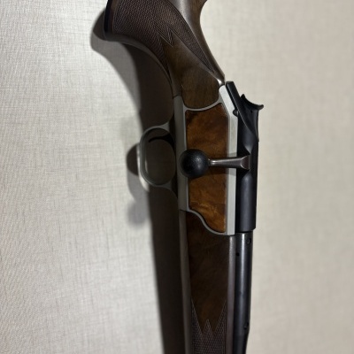 Rifle de caça com madeira escura e metal prateado e preto encostado em parede bege