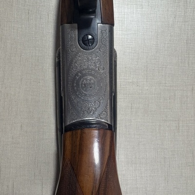 Punho em madeira e corpo metálico gravado de uma arma de fogo Beretta sobre superfície cinzenta.