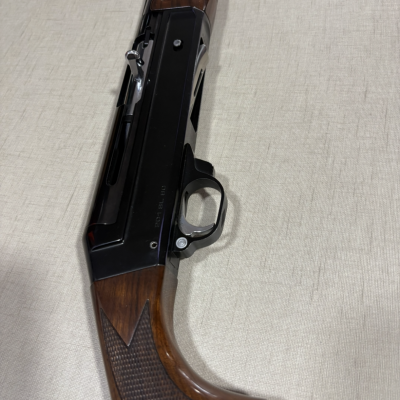 Espingarda com coronha de madeira castanha e corpo metálico preto com inscrições visíveis sobre fundo claro.