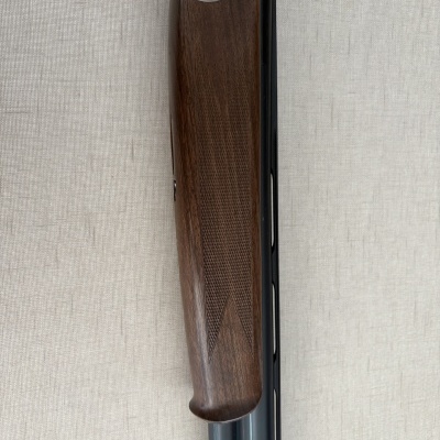 Espingarda Beretta com madeira trabalhada e metal gravado em fundo branco.